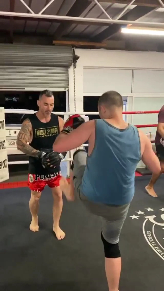 Shaun holding Thai pads while a member throws a kick in the ring